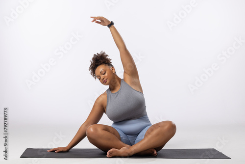A biracial young female plus size model stretches on white background, copy space