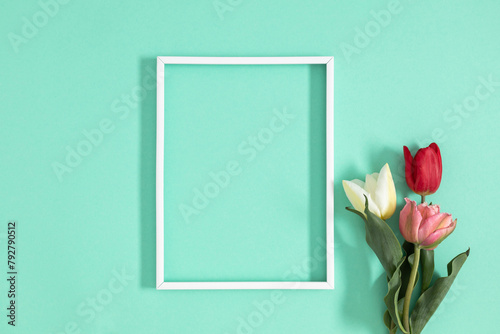 Top view of empty white frame and bouquet of beautiful tulips on mint background. Top view, flat lay.