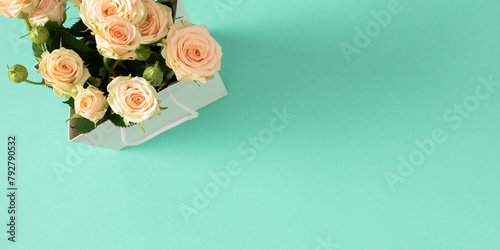 Holiday floral background with white roses on light green background. Gift bag with a bouquet of delicate light roses on mint table background. Top view. Flat lay.