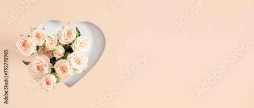 Festive light background with beautiful small roses. White roses and heart frame on pastel beige background. Mother's day, Valentines Day, wedding. Banner