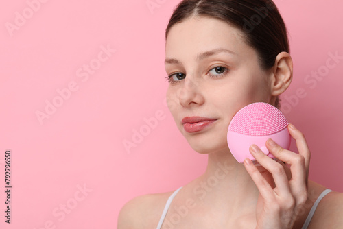 Washing face. Young woman with cleansing brush on pink background, space for text