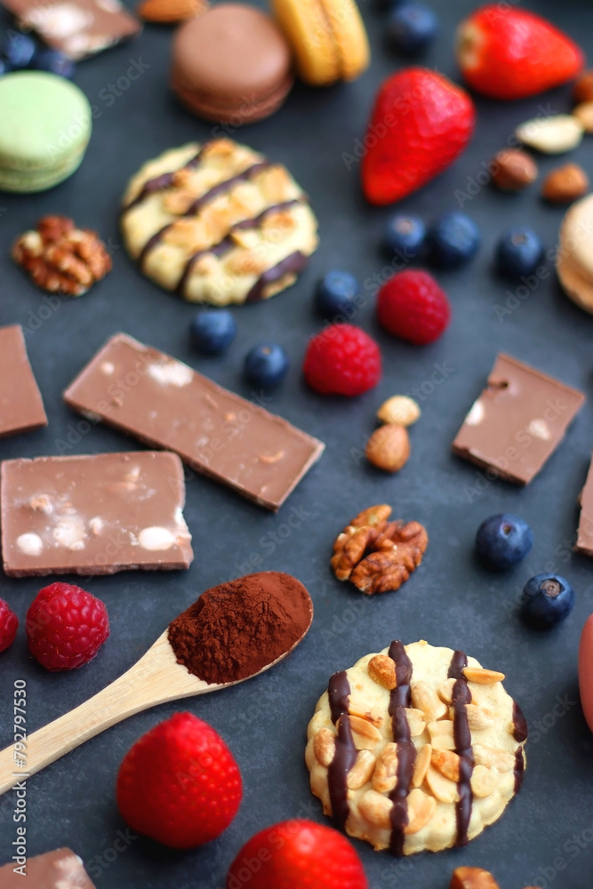 Macarons, chocolate, cookies, berries and various nuts on dark blue background. Selective focus. Macarons, chocolate, cookies, berries and various nuts on dark blue background. Selective focus.