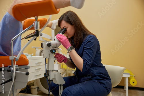 Gynecologist looking in colposcope examining patient on disease photo