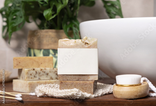 Soap bar with blank label near hygiene products on wood in bathroom close up, mockup