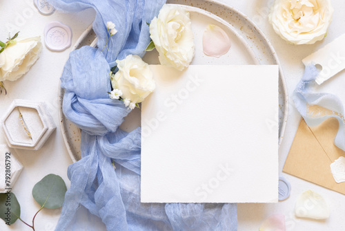 Card near blue tulle fabric knot and cream roses on plates top view copy space, wedding mockup