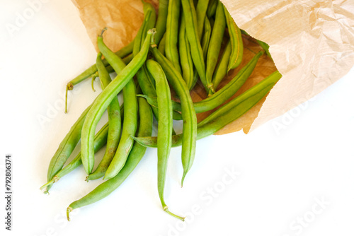 Closeup of organic ripe green bean pods in a brown paper eco bag on a white background. Zero waste environment concept.	