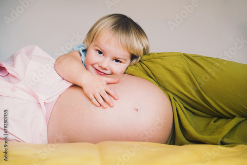Pregnant mother and daughter together at home. Woman with her first child during second pregnancy. Motherhood and parenting concept. Toddler smiling girl and mom. Happy family expecting for new baby.
