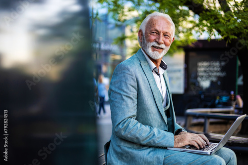 Smiling Caucasian businessman using laptop outdoors. Business man office worker working on urban park background using laptop