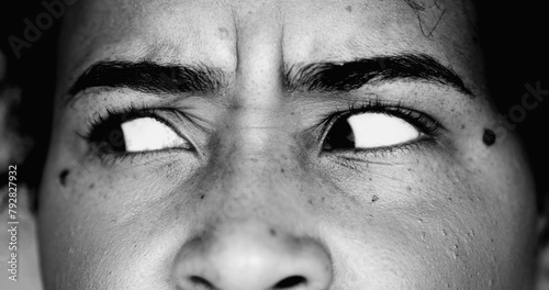 One paranoid worried young black woman macro close-up eyes looking sideways with intense preoccupation and obsession in dramatic black and white monochrome photo