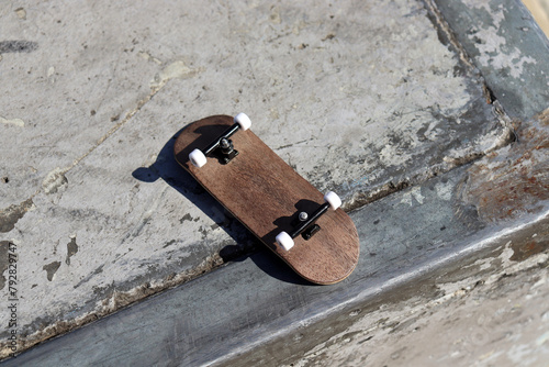 Blank wooden fingerboard at the ramp in concrete skatepark, close up. Mini skateboard, small skateboard deck
