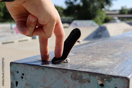 Male hand playing with black wooden fingerboard doing grind or slide trick at the ramp in skatepark, close up. Mini skateboard, small skateboard deck