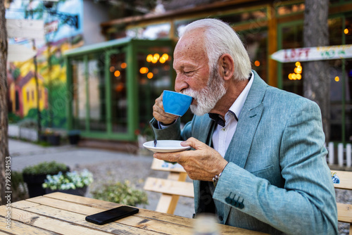 Thoughtful mature man drinking coffee in a cafe and looking away. Portrait of a bearded senior man drinking coffee in a cafe.