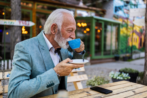 Finding contentment in a cup of coffee, a senior man takes a moment to unwind in the cafe's soothing atmosphere. Senior man drinking coffee at restaurant.