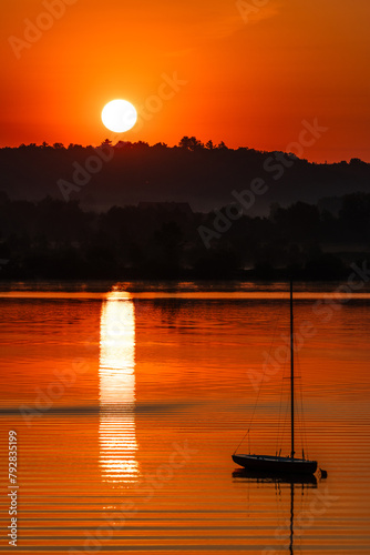 Romantyczny wschód słońca nad jeziorem z jachtem w tle
