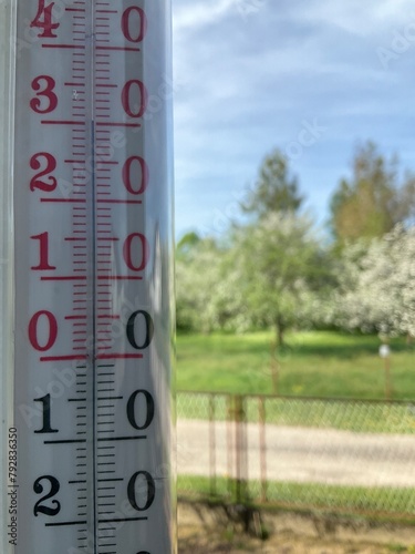 Record high temperature on thermometer in shade outside window in April in southern Poland in 2024. 30 degrees Celsius, blooming trees and blue sky in background. Topics: weather anomalies, spring
