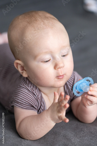 Baby looking with big interest to the blue pacifier. Curious kid.