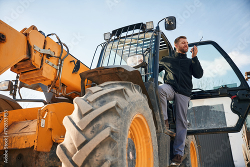 View from below, using walkie talkie. Man is with tractor. Agricultural worker