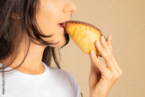 unrecognizable young woman dressed in a white shirt holding an empanada, salteña 
