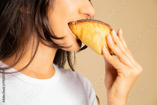 young woman biting into a snack, empanada, salteña, happily enjoying food
