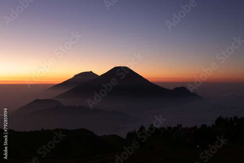 Sunrise on Mount Prau, Central Java, Indonesia. Golden rays appear on the blue horizon with mist shrouding the mountain. photo