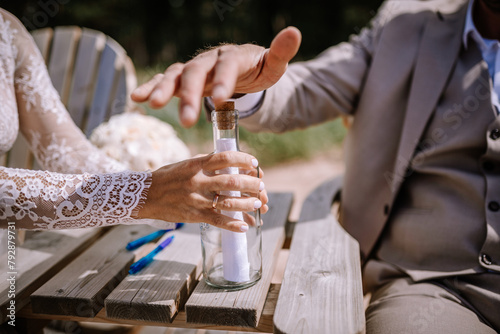 Bild auf Leinwand Valmiera, Latvia - August 10, 2023 - Close-up of a bride and groom's hands placing a note into a bottle on a wooden table