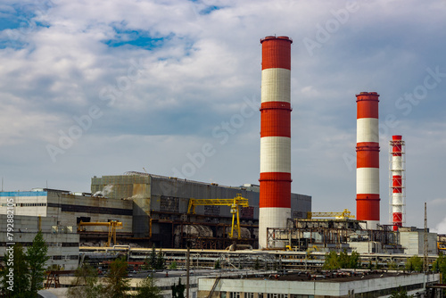 Red and white chimneys of a power plant in Moscow, Russia; greenhouse gas emitting tall chimneys at a power station against a blue sky.