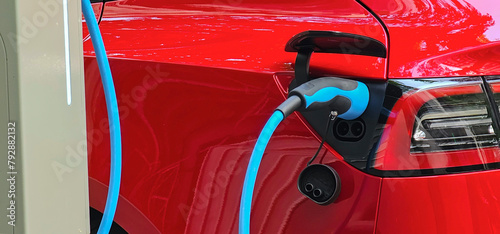 Close up of a red, shiny electric car charging at a street charging station in Europe; concept shot of reducing CO2 emissions by using electric and hybrid cars.