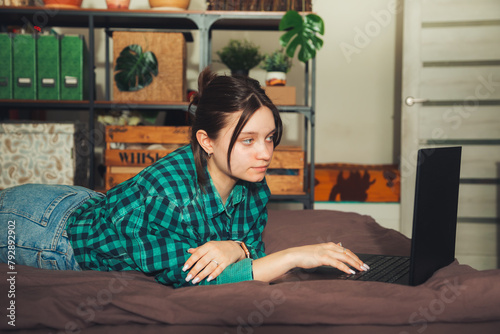 Beautiful young woman working on laptop while lying on bed at home.