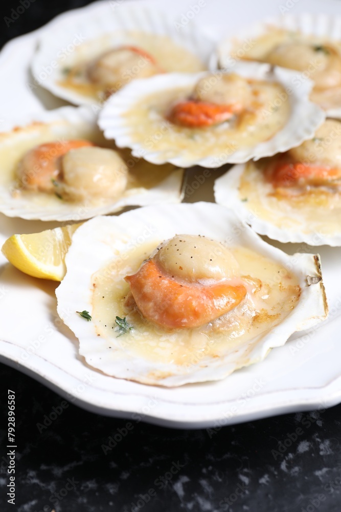 Fried scallops in shells and lemon on black table, closeup