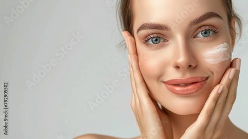 Smiling woman in front of a light background applies facial cream to her cheek with two fingers