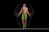 Full-length of muscular, athletic young man in motion, training, jumping rope against black background with stroboscope effect. Concept of sport, active and healthy lifestyle, endurance and strength