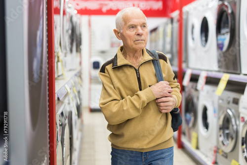 Elderly man choosing washing machine in showroom of electrical appliance store