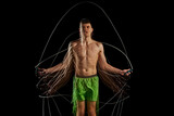 Passion and determination to fitness. Athletic man wit shirt6less muscular body training, jumping rope against black background with stroboscope effect. Concept of sport, active and healthy lifestyle