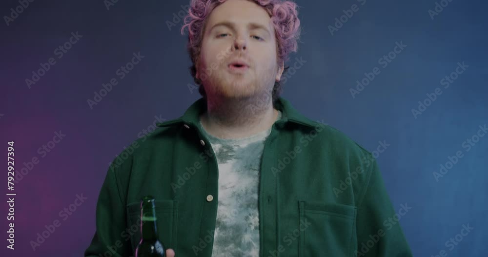 Portrait of brutal young man opening beer bottle with teeth and drinking cold alcohol looking at camera on purple background. Modern lifestyle and alcoholic drink concept. Portrait of brutal young man opening beer bottle with teeth and drinking cold alcohol looking at camera on purple background. Modern lifestyle and alcoholic drink concept.