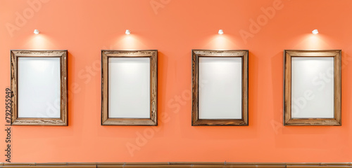 Four empty frames with vintage wood finishes on a pastel orange wall, illuminated by subtle gallery lighting photo