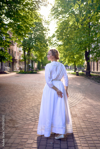 chic middle age woman in a white vintage dress in a sunlit alley