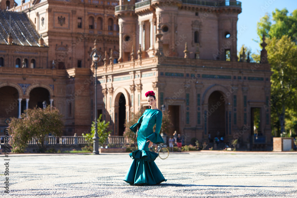 Young and beautiful woman with typical green dress with ruffles and dancing flamenco in plaza de espana in seville, andalusia, walks with art and passion. 16 november, international flamenco day.