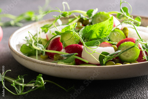 Fresh spring salad with red radish, cucumber,aromatic herbs and olive oil on black stone table close up. Healthy diet food concept.