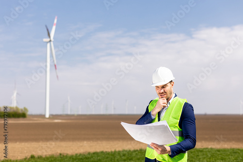 Smiling Engineer Reviewing Plans Near Wind Turbines on a Sunny Day. Generative AI