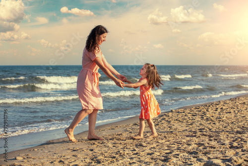 Young happy woman with a little daughter holding hands and dancing on the beach