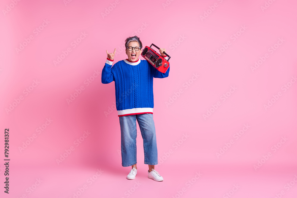 Full size portrait of nice aged lady boombox show heavy metal symbol wear blue sweater isolated on pink color background Full size portrait of nice aged lady boombox show heavy metal symbol wear blue sweater isolated on pink color background