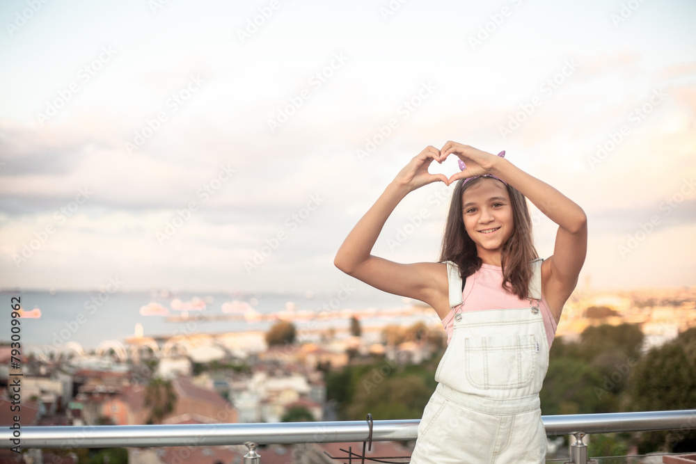 Portrait of a beautiful girl against the background of the roofs of the city. The model makes heart