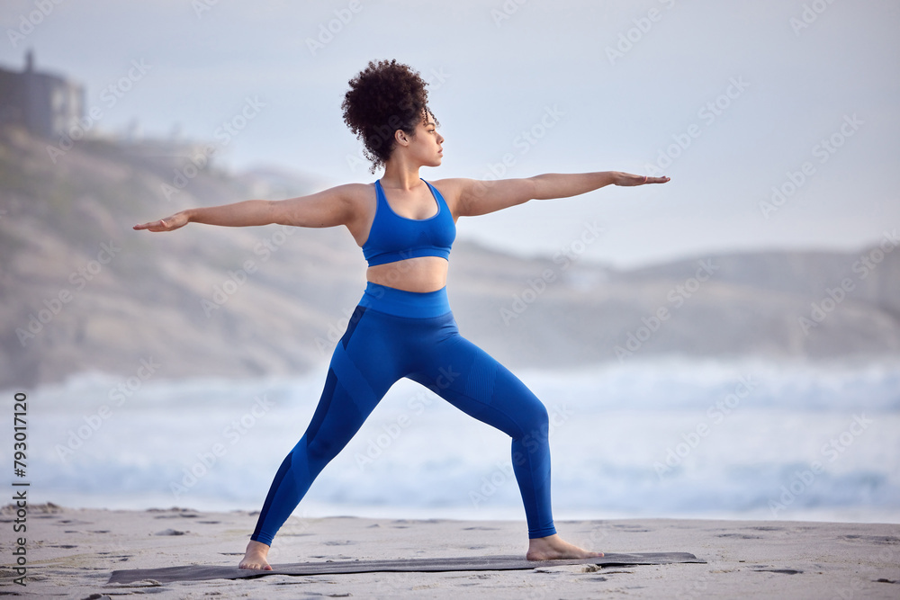 Black woman, yoga and fitness for wellness at beach with peaceful mind, warrior pose and body. African person, zen and pilates workout at sea with stretching, spirituality and balance with training