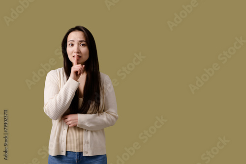 Scared asian woman showing silience gesture isolated on green 