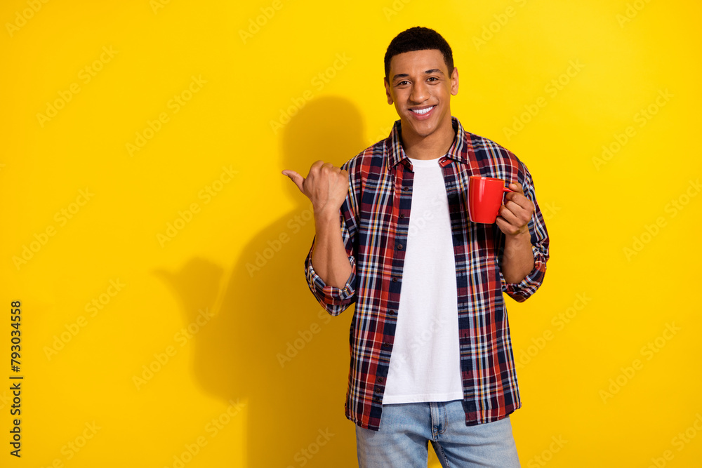 Photo of attractive cheerful man wear trendy clothes hold mug recommend tasty drink empty space isolated on yellow color background