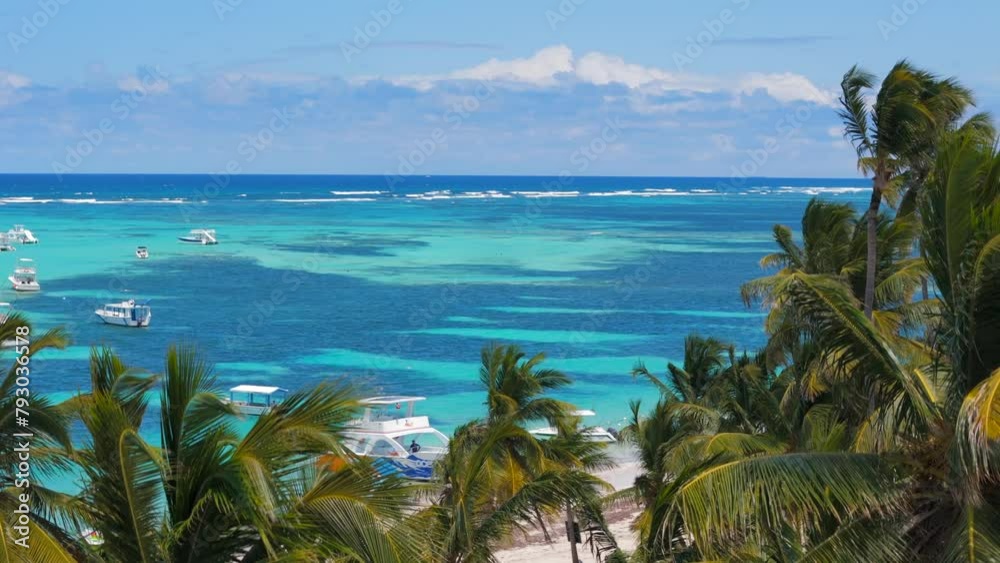 Aerial flight above palm trees on the white sand beach and turquoise water of the Caribbean Sea. Many excursion yachts and fishing boats anchored near the all inclusive resorts in Punta Cana