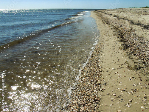 Sea waves are rolling onto the shore of the summer beach covered with small stones