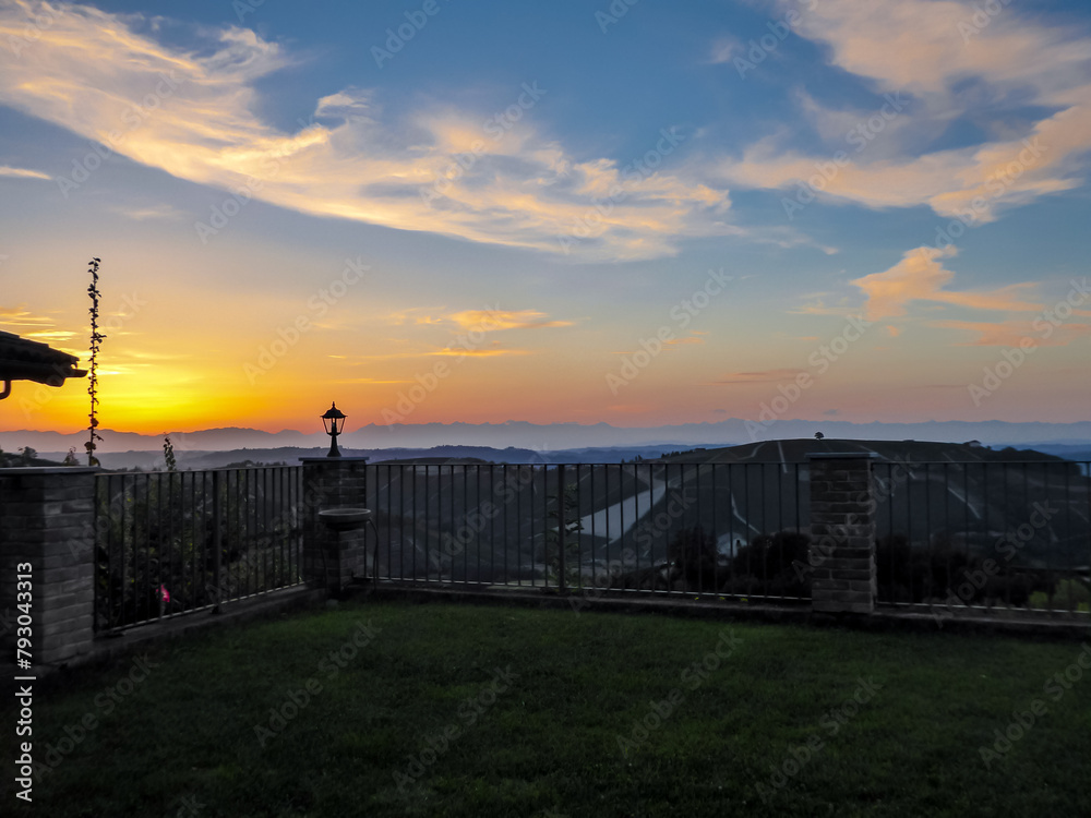 Watching sunset from private terrace on remote vineyard in Langhe wine region of Piedmont (Piemonte), Italy, Europe.  Luxury get away vacation. Romantic atmosphere. Alps mountain range in background