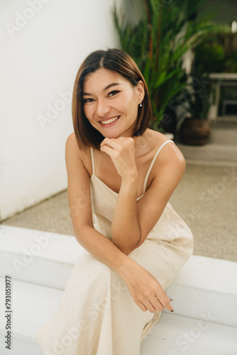 Attractive asian woman in a beige dress is sitting outdoors