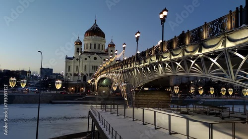 Side view of Cathedral of Christ the Saviour next to illuminated bridge at winter twilight in Moscow, Russia. Slow motion handheld video. Russian culture. Religious architecture theme.